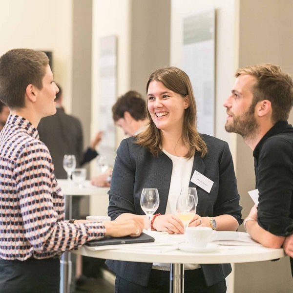 Drei Personen am Stehtisch in einer Unterhaltung.