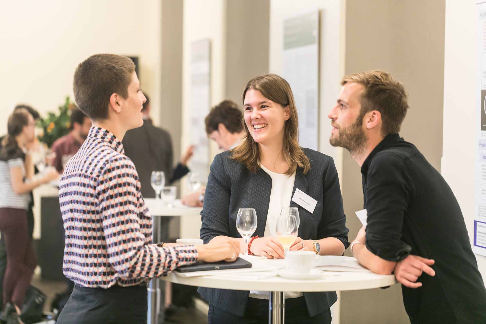 Drei Personen am Stehtisch in einer Unterhaltung.