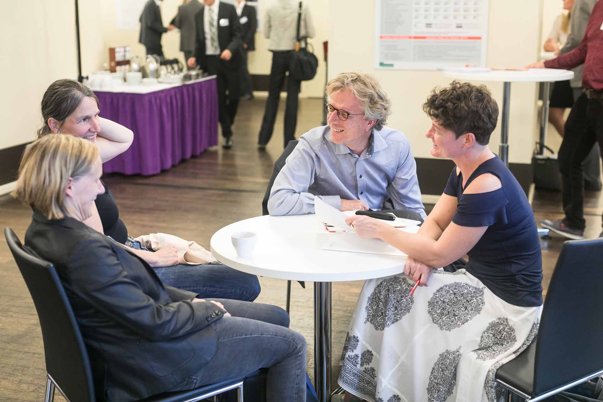 Vier Personen sitzen an einem Tisch, unterhalten sich und lachen.